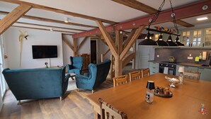 A spacious living area with a wooden ceiling, a blue sofa, a dining table with chairs, and a kitchen in the background. - Historic horse stable in the center of Weißenburg (Weißenburg in Bayern)