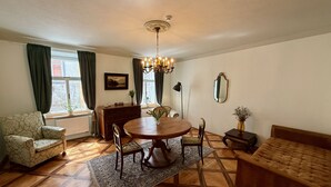 A dining area with a round table, chairs, a chandelier, a sofa, and a window with curtains. - Mini-Teater Suites - Apartment 1  - sleeps 3 guests  in 1 bedroom (Ljubljana)