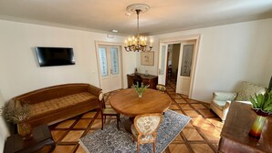 A dining area with a round wooden table, a sofa, and a TV mounted on the wall. - Mini-Teater Suites - Apartment 1  - sleeps 3 guests  in 1 bedroom (Ljubljana)