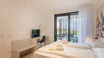 A hotel room with a bed, a desk, a television, and a view of a building through the window.