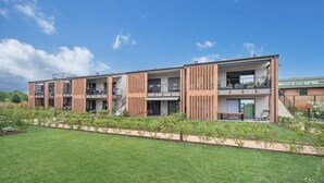 Ein modernes, mehrgeschossiges Gebäude mit Balkonen, einer flachen Dachterrasse und einem gepflegten Rasen.
