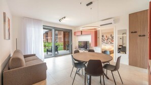 Ein modernes Wohnzimmer mit einer Couch, einem Esstisch mit Stühlen, einem Fernseher und einer Glastür, die zu einem Außenbereich führt.