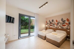 Habitación de hotel con un gran ventanal corredero a un jardín, un televisor de pantalla plana en la pared y una cama con cabecero decorado con un diseño de hojas.