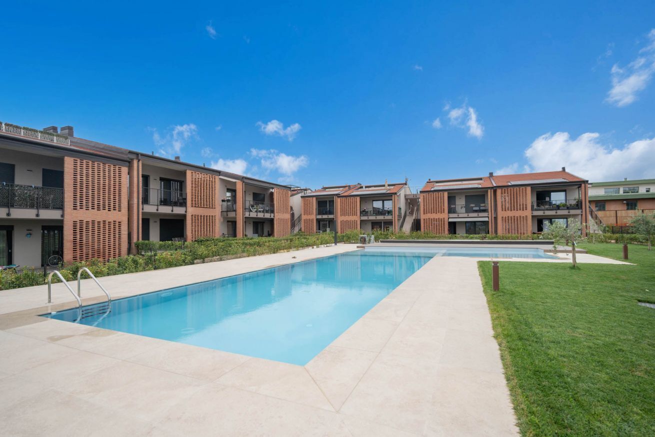 A modern residential building with a swimming pool, balconies, and a clear blue sky.