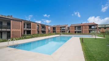 A modern residential building with a swimming pool, balconies, and a clear blue sky.