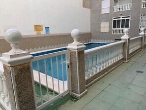 Una piscina con cerco blanco y columnas, suelo de baldosas y un edificio con balcones.