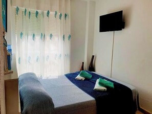 Une chambre à coucher avec un lit, un téléviseur à écran plat fixé au mur et une fenêtre avec des rideaux.