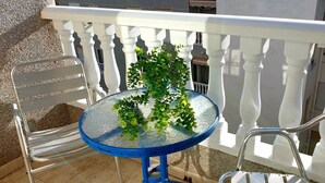 A balcony with a white railing, a round table with a glass top, and two metal chairs. - Torrevieja apartment next to the beach (Torrevieja)