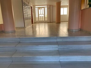Un pasillo con escalones de mármol que conducen a una puerta, columnas y piso de baldosas.