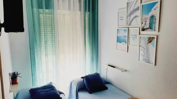 A room with two beds, a window with sheer curtains, and a wall with framed pictures. - Torrevieja apartment next to the beach (Torrevieja)