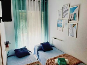 Une chambre avec deux lits, une fenêtre avec des rideaux légers et un mur orné de tableaux.
