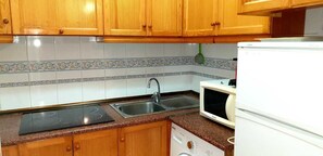 Una cocina con armarios de madera, un lavamanos, una estufa, un microondas y una lavadora.