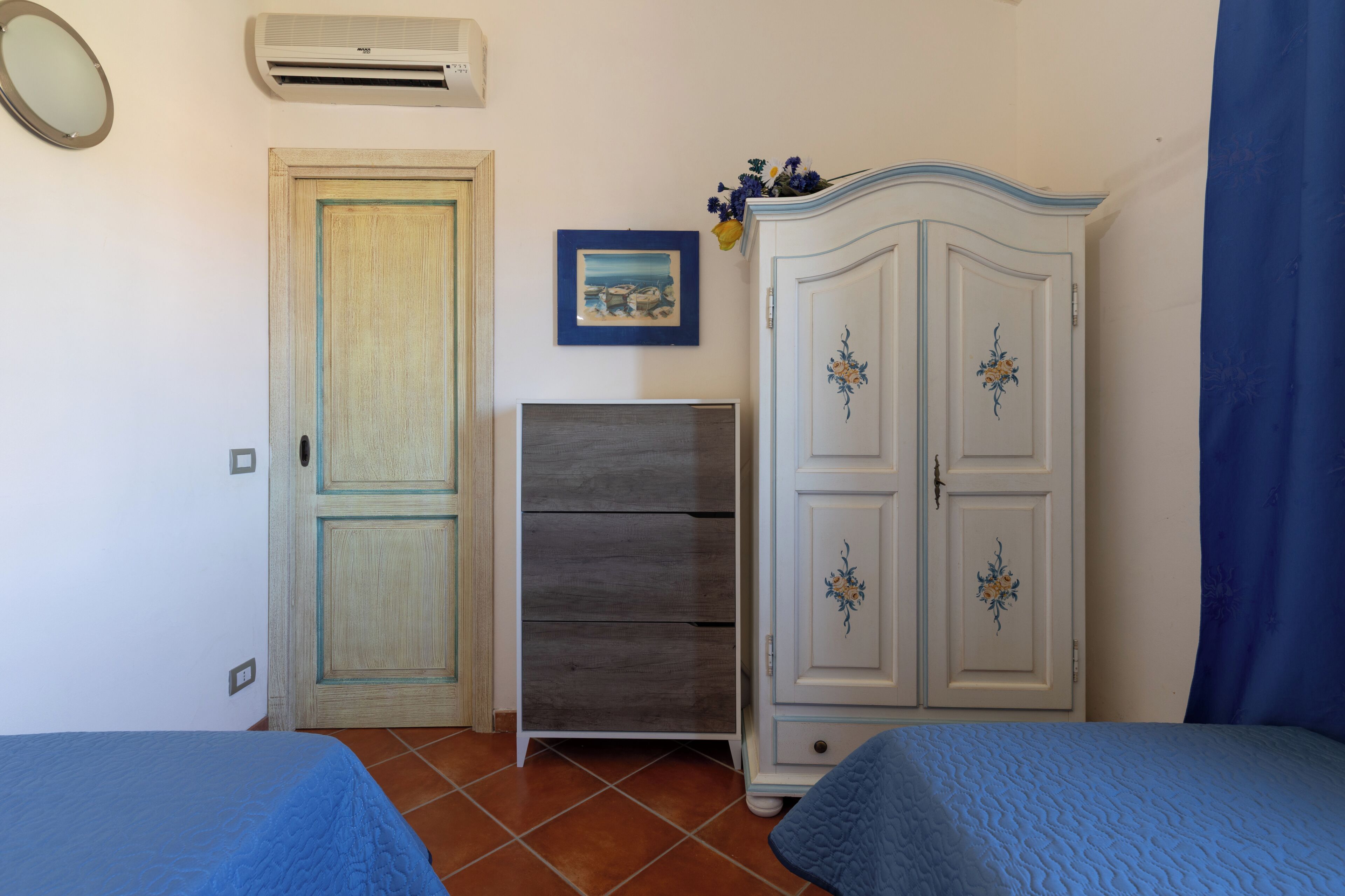 A bedroom with two beds, a wardrobe, a dresser, a mirror, and an air conditioner.
