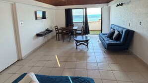 A room with a brick ceiling, a bed, a sofa, a dining table with chairs, and a TV on the wall. - Beachfront apartment (Cancún)