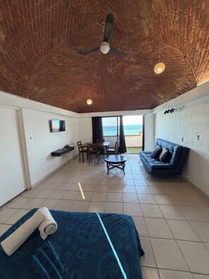 Ein Zimmer mit Ziegeldecke, einem Bett, einem Sofa, einem Esstisch mit Stühlen und einem Fernseher an der Wand.