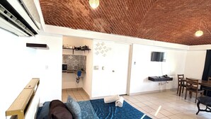 A room with a brick ceiling, a bed with a blue patterned bedspread, a desk with a chair, and a television on the wall. - Beachfront apartment (Cancún)