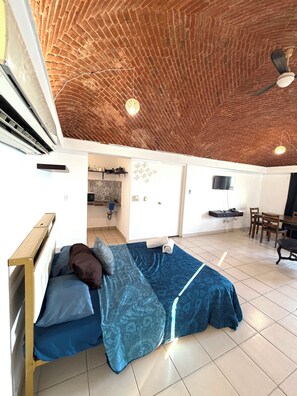 Ein Zimmer mit Ziegeldecke, einem Bett mit blauem Muster, einem Schreibtisch mit Stuhl und einem an der Wand befestigten Fernseher.