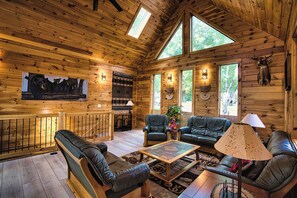 Ein Blockhaus-Interieur mit Holzbalkendecke, Kamin, Ledersofas, einem Couchtisch und einem großen Fenster.
