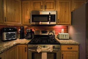 A kitchen with wooden cabinets, a stainless steel microwave, a coffee maker, a toaster, and a gas stove. - Psalm 27 05 Relaxing Smoky Mountain Cabin | 3 Bedrooms, 4 Baths, Sleeps 10 (Sevierville)