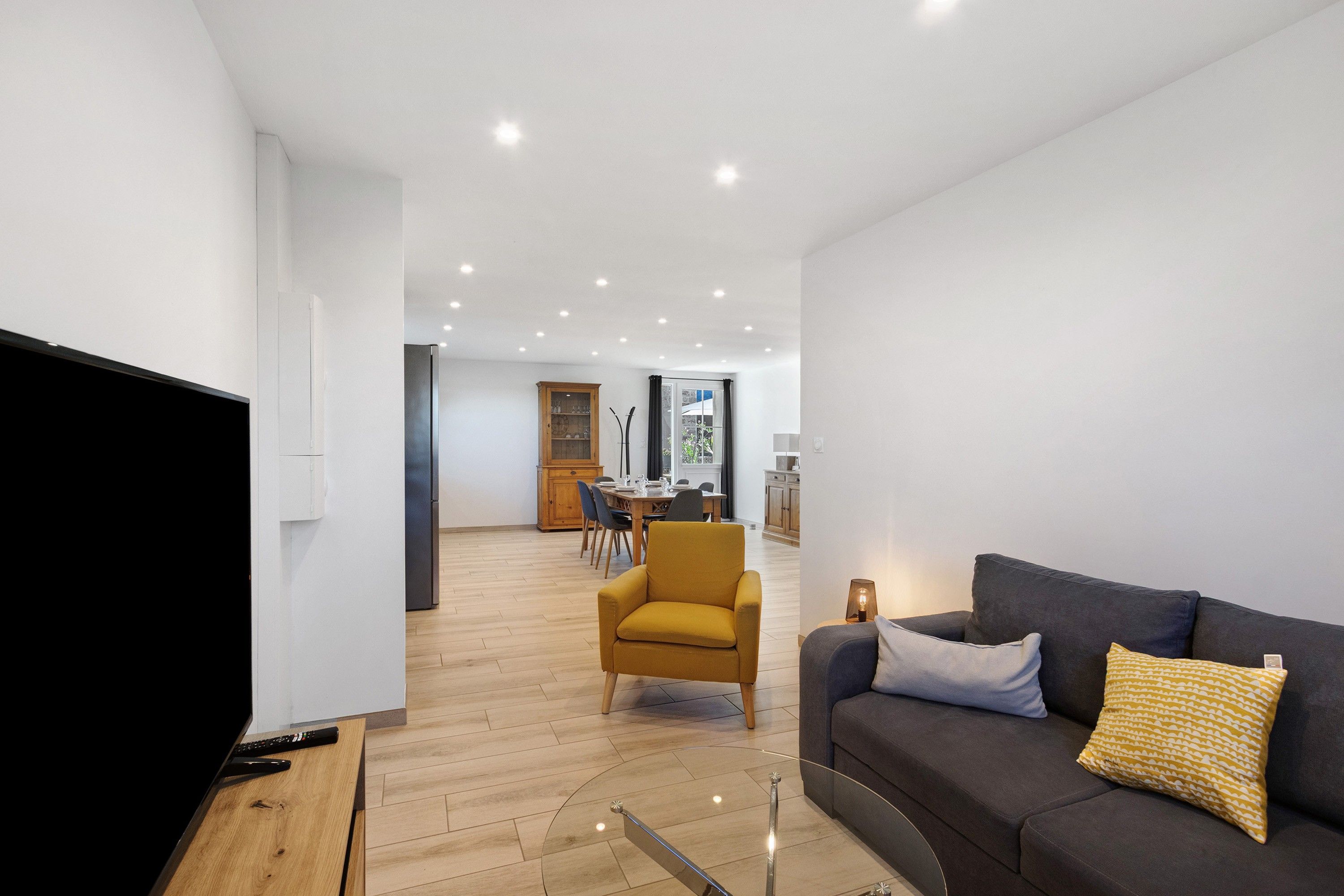 A modern living room with a flat-screen TV, a sofa, and a dining area in the background.