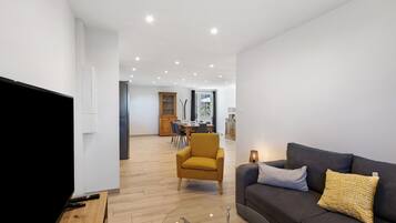 A modern living room with a flat-screen TV, a sofa, and a dining area in the background.
