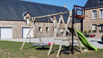 Een houten schommel met een glijbaan, een basketbalveld en een garage op de achtergrond.
