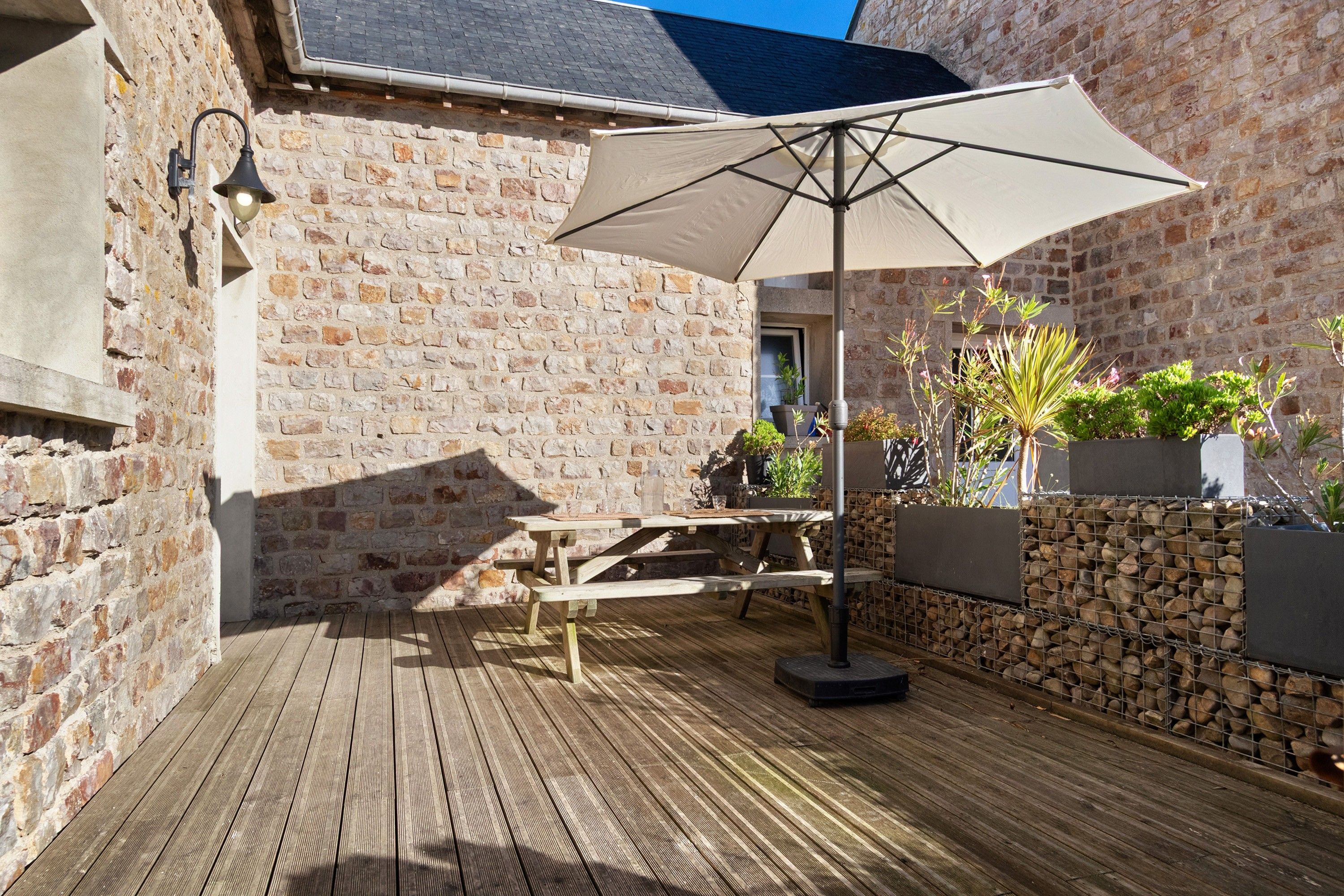 A wooden deck with a picnic table and umbrella, surrounded by stone walls and potted plants.