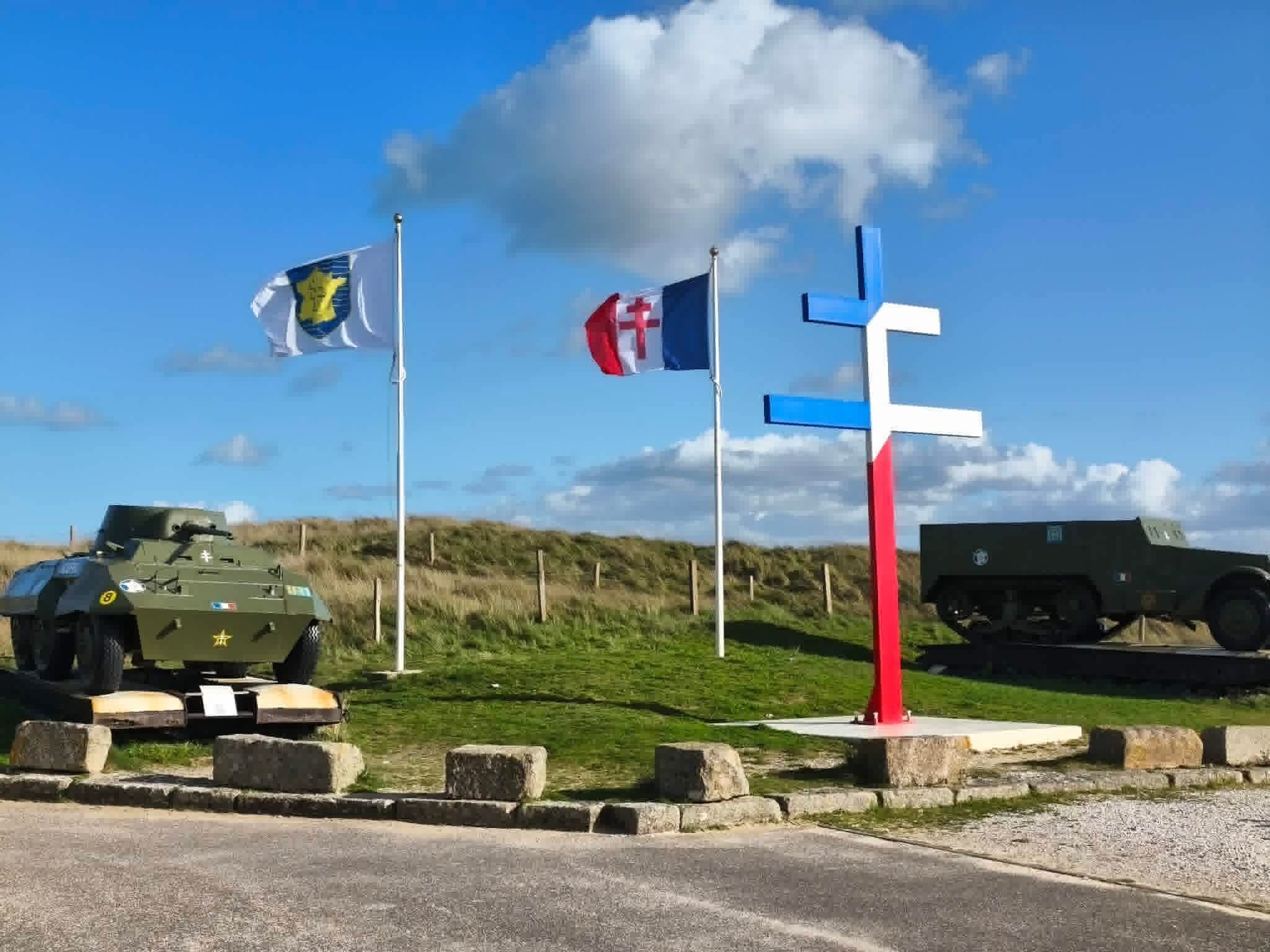 Un véhicule militaire est garé sur une route, et un mât porte plusieurs drapeaux.