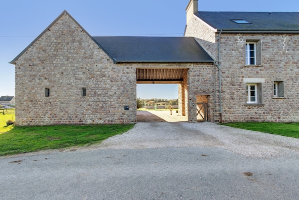 A stone building with a gravel driveway leading to a wooden gate.