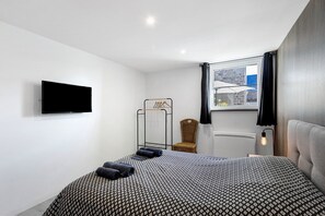 A modern bedroom with a bed, a television, a window with a view, and a chair. - Gite 'Domaine de la dune' between land and sea (Saint-Germain-de-Varreville)
