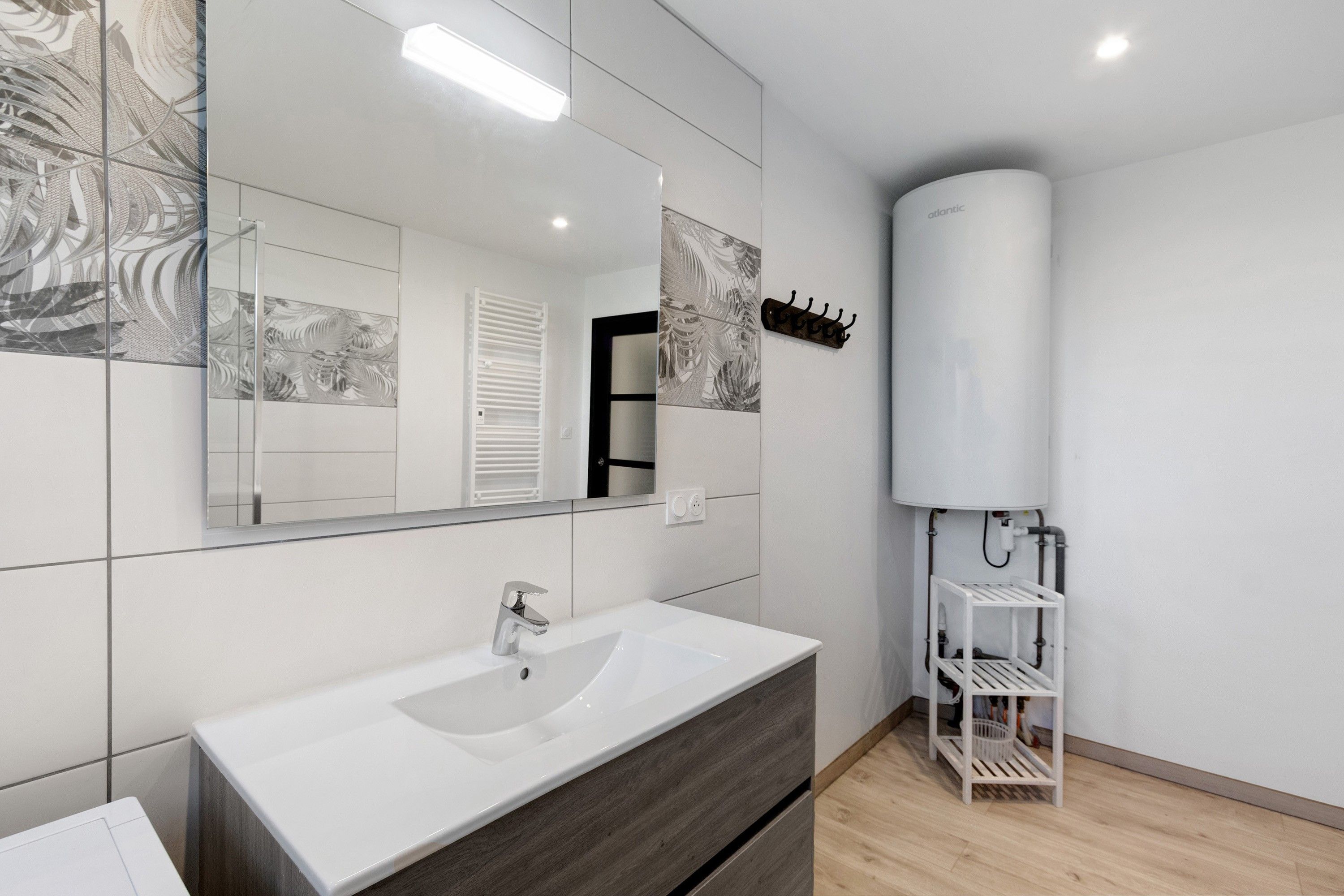 A modern bathroom with a white sink, a large mirror, and a towel rack.
