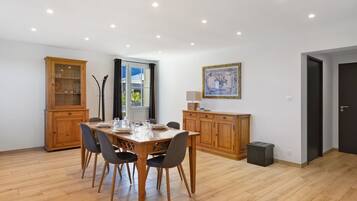 Un coin repas avec une table en bois dressée pour quatre personnes, bordée de meubles en bois, une fenêtre avec des rideaux et un tableau encadré au mur.