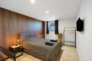 Quarto moderno com cama grande, mesas de cabeceira, guarda-roupa e janela com cortinas.