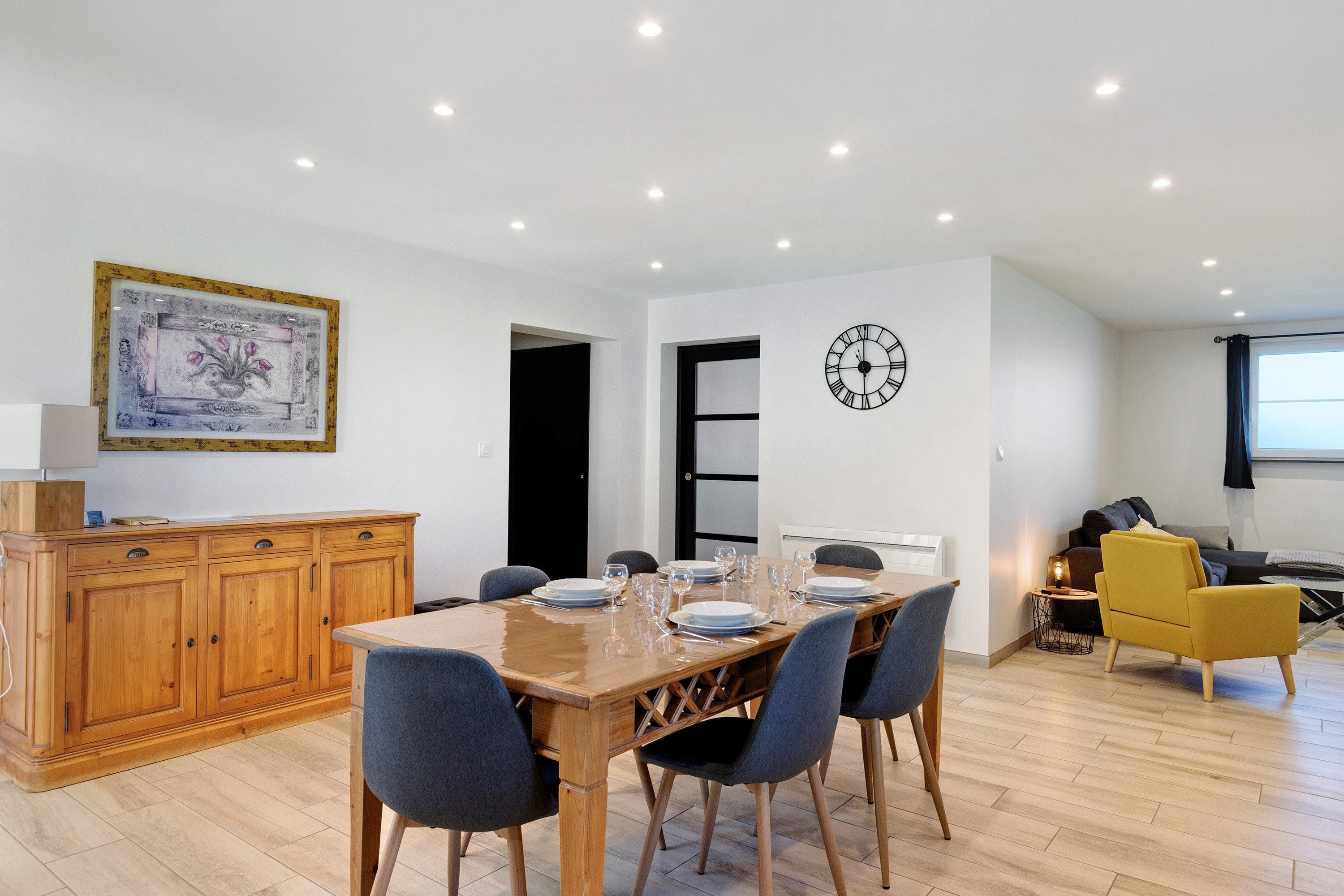 Un coin repas avec une table en bois, dressée pour quatre personnes, entourée de chaises.