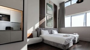 Ein modernes Hotelzimmer mit Küchenzeile, einem großen Bett, zwei Nachttischen und Blick auf die Stadt.