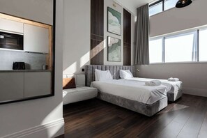 Ein modernes Hotelzimmer mit Küchenzeile, einem großen Bett, zwei Nachttischen und Blick auf die Stadt.