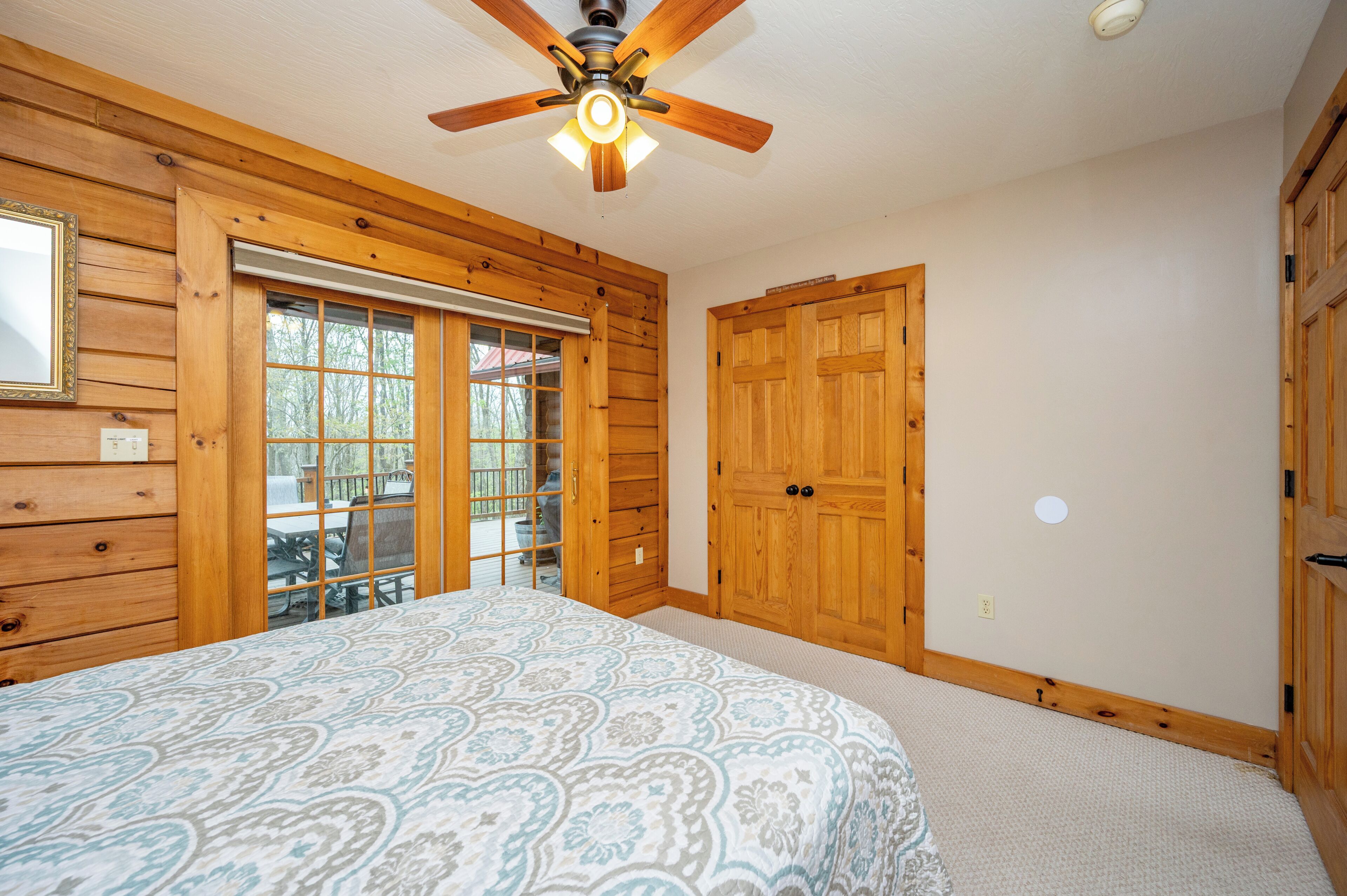 A bedroom with a bed, wooden walls, a ceiling fan, and a sliding glass door leading to an outdoor area.