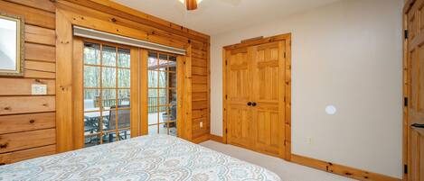 A bedroom with a bed, wooden walls, a ceiling fan, and a sliding glass door leading to an outdoor area.