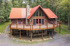 A log cabin with a deck, large windows, and a stone chimney. - New! Dog Friendly Mountain Retreat w/Hot Tub (McHenry)