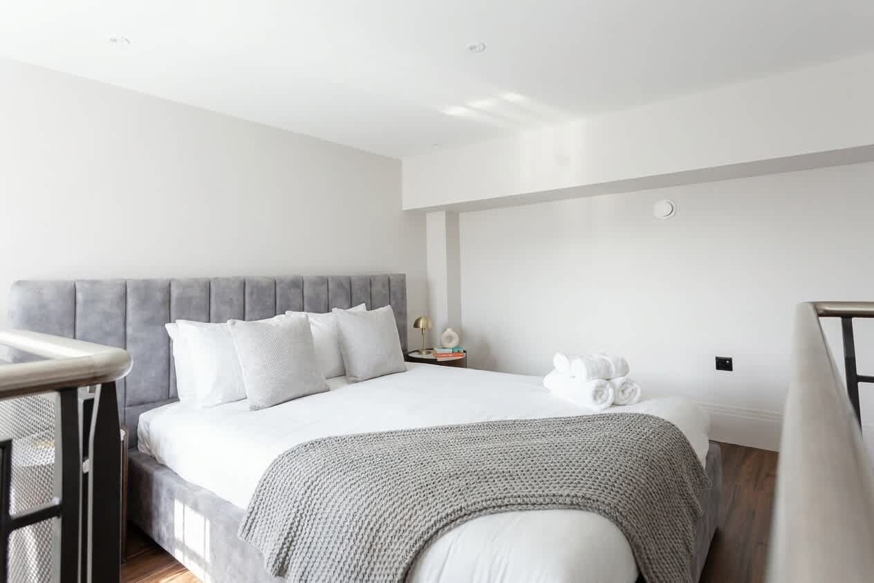 A modern hotel room with a large bed, a bedside table, and a small nightstand.