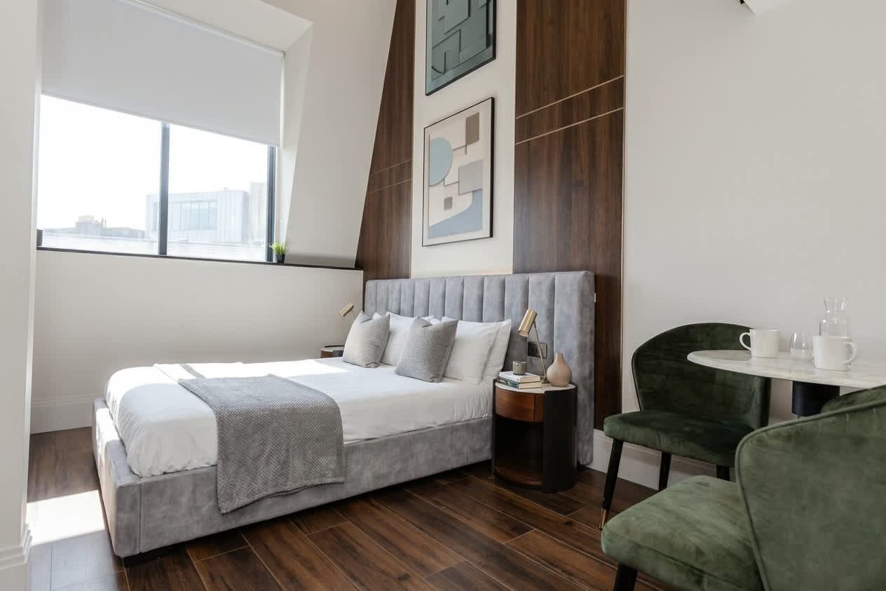 Ein modernes Schlafzimmer mit Bett, Nachttisch, Stuhl und Blick auf die Stadt.
