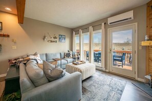 Ein Wohnzimmer mit einer Couch, Hocker und einem großen Fenster mit Vorhängen.