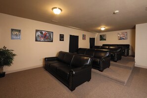 Ein Heimkino mit einer schwarzen Ledersofa, mehreren schwarzen Ledersesseln und Wandlautsprechern.