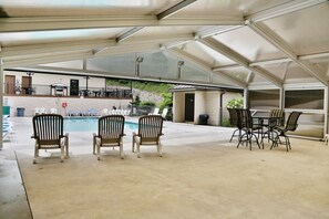 Et overdækket udendørsområde med swimmingpool, liggestole og et bord med stole.