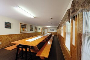Ein langer Holztisch mit weißer Tischdecke, Holzwänden und einem Fenster mit Jalousien.