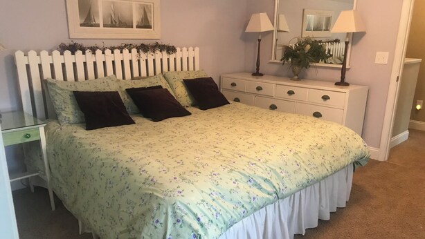 Een slaapkamer met een bed, een dressoir, een nachtkastje, een spiegel en een aan de muur hangend schilderij.