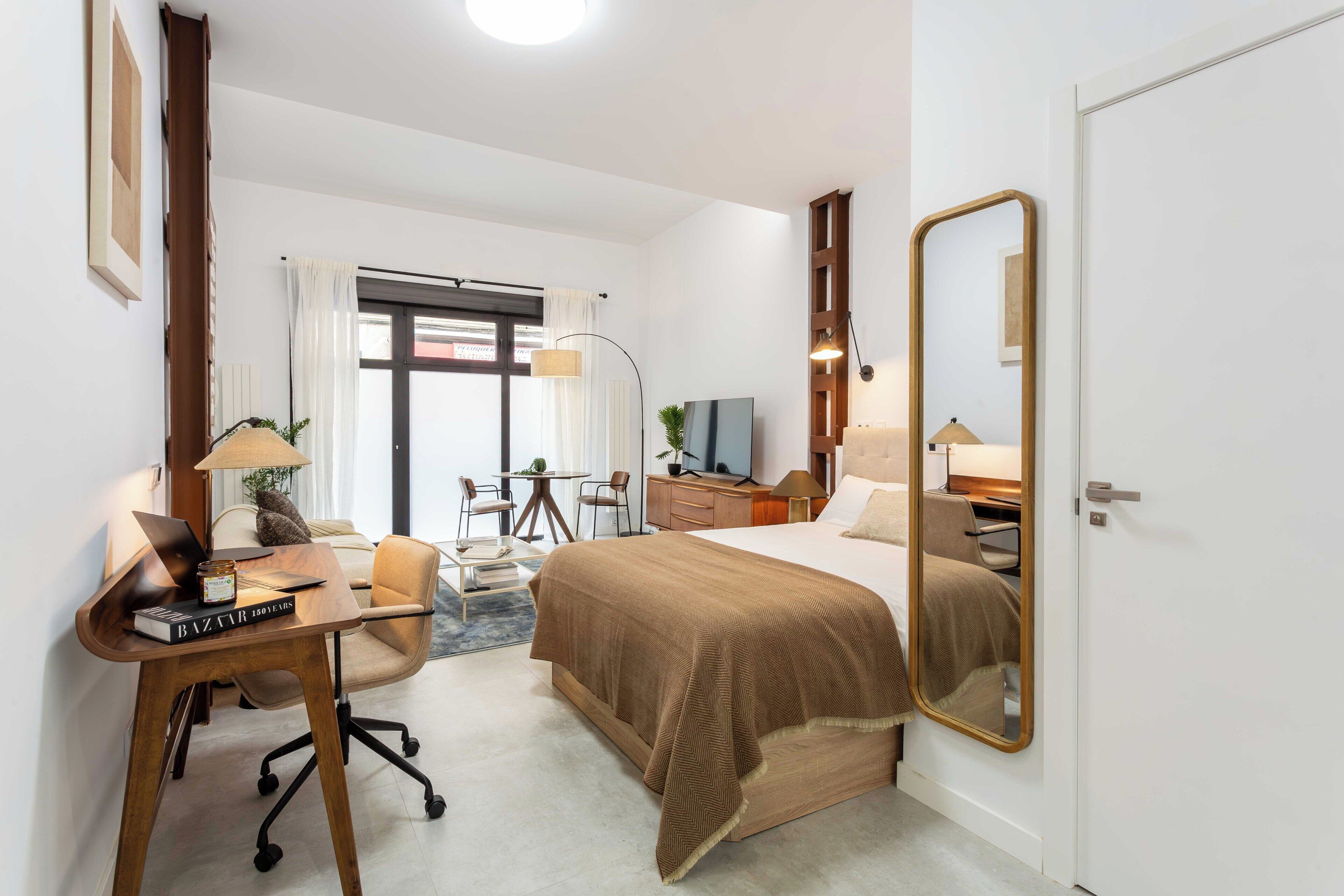 A hotel room with a bed, desk, chair, lamp, and a large mirror.
