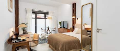 A hotel room with a bed, desk, chair, lamp, and a large mirror.