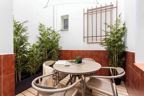 A round table with four chairs, a small potted plant, and a window with a shutter. - A spacious furnished studio in the heart of Tetuán with its own private patio, for slow coffee in the morning or a workday in the sun. (MADRID)