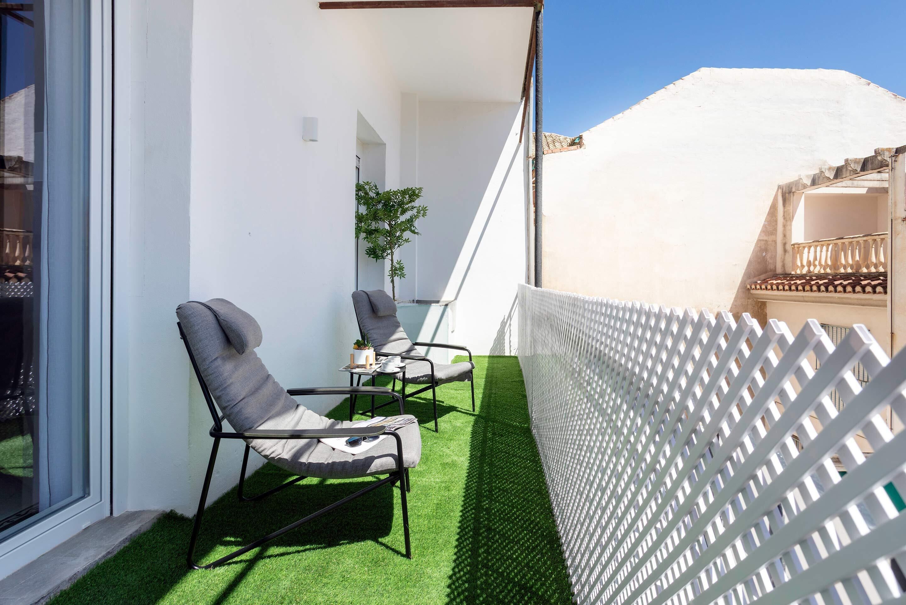 A balcony with two lounge chairs, a small table, and a potted plant.
